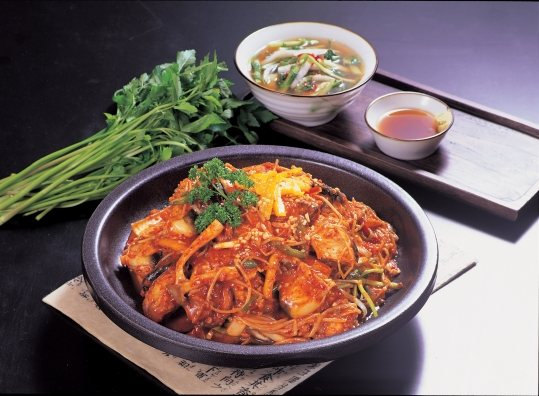 검은 냄비에 콩나물과 채소를 넣은 붉은 양념 찜 — 위에 파슬리·채 썬 달걀지단, 왼쪽에 미나리 한 단, 뒤에 맑은 국 한 그릇과 소스 종지